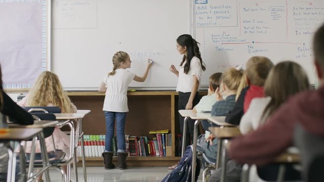 Teacher watching girl solving math equation on classroom whiteboard / Provo, Utah, United States