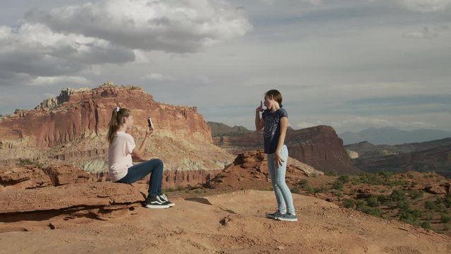 Girl photographing friend in scenic view of desert landscape with cell phone / Capitol Reef National Park, Utah, United States