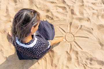 Girl draws on the sand with her finger.