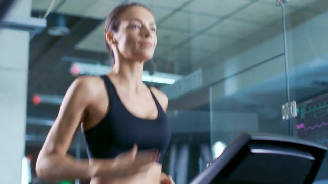 Beautiful Woman Athlete Wearing Sport Bra, Walks on a Treadmill, Training Exercise. In the Background Modern Gym/ Fitness Club.