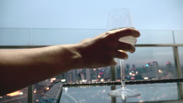 Happy woman drinking a glass of white wine while sitting in rooft bar in the city or on the terrace with cityscape at sunset. Vacation,happiness,freedom concept.