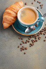 Cup of fresh coffee with croissant on concrete background, selective focus, copy space.