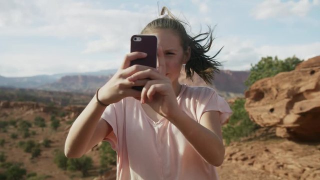 Girl in windy desert photographing scenic view by panning cell phone / Capitol Reef National Park, Utah, United States