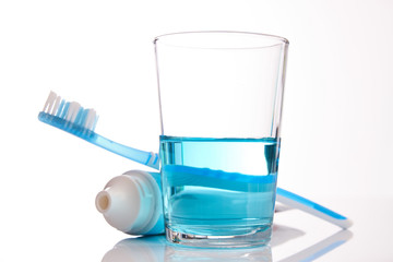 A blue toothbrush with toothpaste and glass of blue mouthwash isolated on white background with copy space, close-up. Dental oral hygiene concept