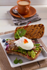 Poached egg, bacon, smashed white bean and avocado on toast. Sandwich. vertical