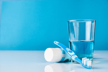A blue toothbrush with toothpaste and glass of blue mouthwash on blue background with copy space, close-up. Dental oral hygiene concept - obrazy, fototapety, plakaty