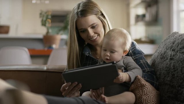 Panning shot of mother and baby daughter reading digital tablet in livingroom / Alpine, Utah, United States
