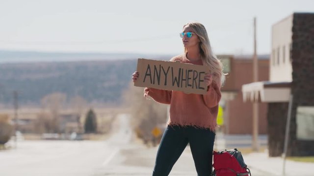 Car picking up woman holding anywhere sign hitchhiking on remote rural road / Loa, Utah, United States