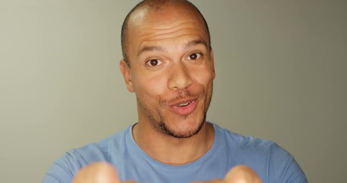 4K Smiling man pointing into camera lens & giving thumbs up on a plain background. Slow motion.