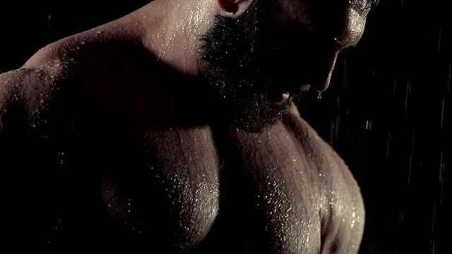 naked chest of young man with inflated muscles, water is dropping from his body in darkness