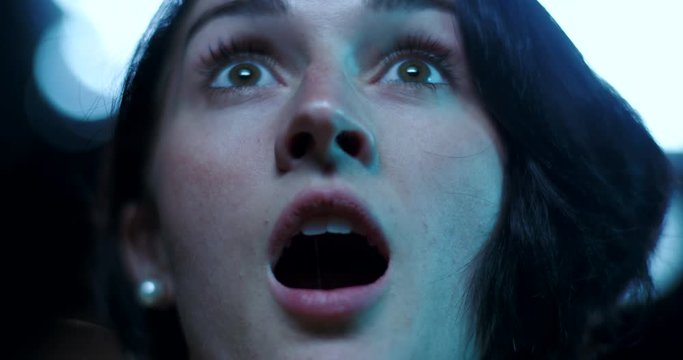Low angle, a surprised look on a young woman's face as she watches a movie