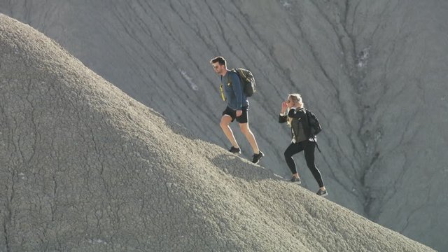 Tracking shot of couple carrying backpacks hiking up mountain / Caineville, Utah, United States