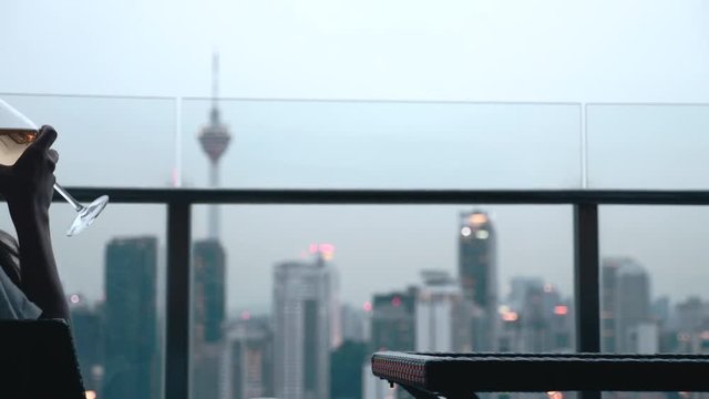 Happy woman drinking a glass of white wine while sitting in rooft bar in the city or on the terrace with cityscape at sunset. Vacation,happiness,freedom concept.