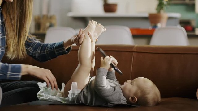 Mother changing diaper of baby daughter distracted with cell phone / Alpine, Utah, United States