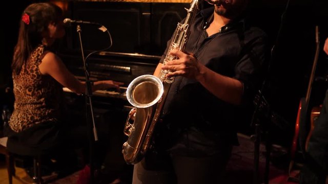 Saxophone player live in nightclub with pianist in the background.