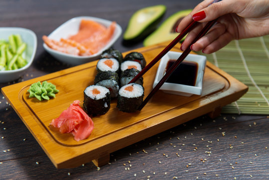 Woman takes the sushi rolls using chopsticks. Black background