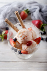Several scoops of strawberry ice cream with wafer, strawberry and blue berry in glass against white wooden table. Summer background. View from above.