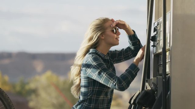Woman using credit card and pressing buttons at windy fuel pump / Hanksville, Utah, United States