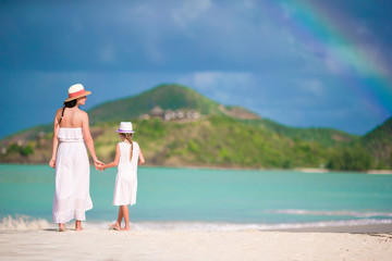 Fototapeta na wymiar Beautiful mother and daughter on Caribbean beach with amazing rainbow on background