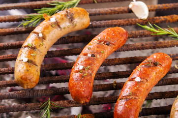Close up of three grilling sausages on barbecue grill with some species. BBQ in the garden. Bavarian sausages