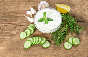 Obraz na płótnie Canvas Tzatziki ingredients wooden kitchen table Yoghurt herbs vegetables