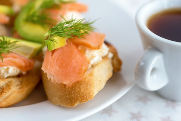 Bruschetta, snack sandwiches with white cheese, smoked salmon and pieces of avocado decorated by dill.