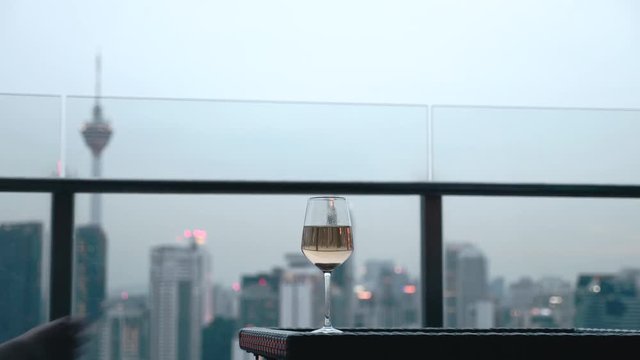 Happy woman drinking a glass of white wine while sitting in rooft bar in the city or on the terrace with cityscape at sunset. Vacation,happiness,freedom concept.