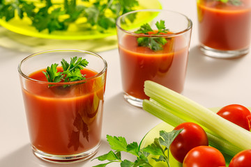 Three glasses of tomato juice decorated with parsley or coriander leaves. Next is a plate of parsley, tomatoes and celery stems