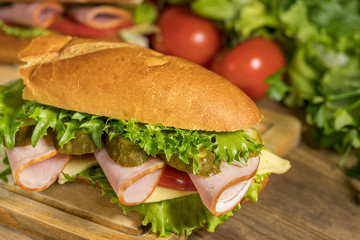 A sandwich with cheese, ham, lettuce, tomatoes and pickled cucumbers lies on a wooden table