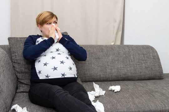 Schwangere Frau ist erkältet und putzt sich die Nase