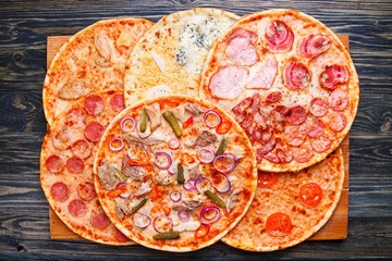 Many pizzas with assorted toppings on rustic wooden table, top view. Food background