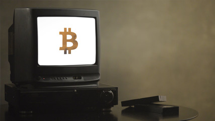 Vintage television on wood table with bitcoin. Old TV showing bitcoin. Near the TV there are film...