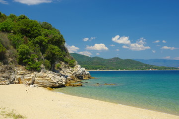 Sea coast near Stagria, Greece. The sandy beach ended with a cliff. A blue sky with white clouds can be seen above the azure sea.