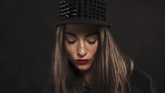 Young attractive caucasian brunette girl with red lipstick in spiked snapback cap portrait on black background