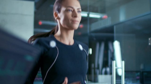 Beautiful Woman Athlete Walks on a Treadmill with Electrodes Attached to Her Body, while Scientist Supervises Her EKG Data Showing on Laboratory Monitors.