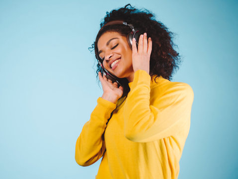 Lifestyle Concept. Portrait of beautiful african american woman joyful listening to music on mobile phone. Blue pastel studio background. Copy Space.