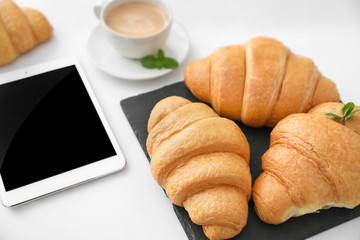 Slate plate with tasty croissants, tablet computer and cup of coffee on table