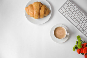 Tasty croissant, cup of coffee and keyboard on light background