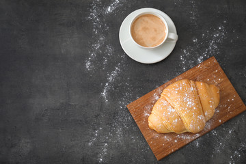 Board with tasty croissant and cup of coffee on table, top view