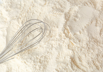 Metal whisk on white wheat flour, top view