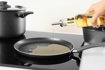 Woman pouring cooking oil from bottle into frying pan on stove