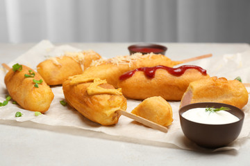 Tasty corn dogs with sauces on table