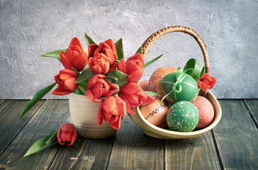 Easter still life. Red tulips and a basket of red and green Easter eggs on dark rustic wood