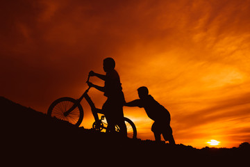 silhouette boys riding bicycle at sunset or sunrise background