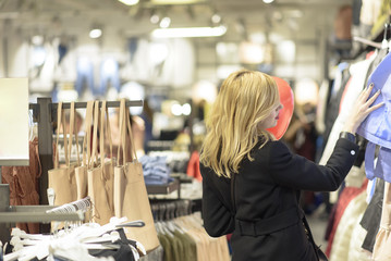 Beautiful blonde young woman choosing some clothes on discount in a boutique, holding a heart shaped balloon for valentine's day