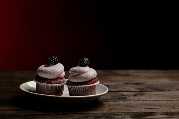 berry cupcakes with blackberry on a white plate on a dark wooden background
