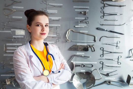 Portrait Of A Doctor On A Stand Background With A Surgical Instrument. Concept Young Student Girl Studying A Medical Tool