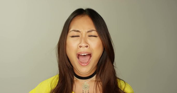 4K Close up beautiful Asian girl doing a big yawn to camera on grey background. Slow motion.