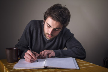 Young student solving math problems or writting an essay in his notebook and drinking coffee