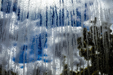Glass window with rain, sky clouds and sun on background